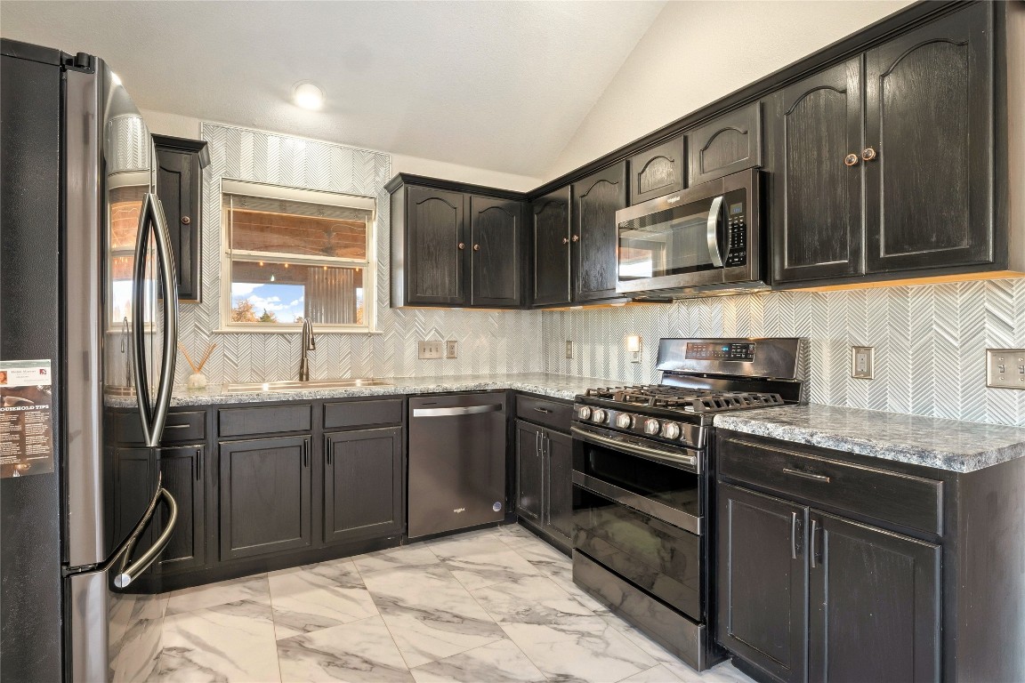 167 Hay Meadow Road Cedar Creek, TX 78612 - Photo 12 of 39 Kitchen with vaulted ceiling, stainless steel appliances, light tile floors, decorative backsplash, and light stone counters