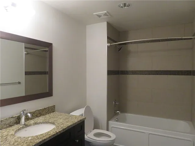 a bathroom with a granite countertop bathtub shower sink vanity and toilet