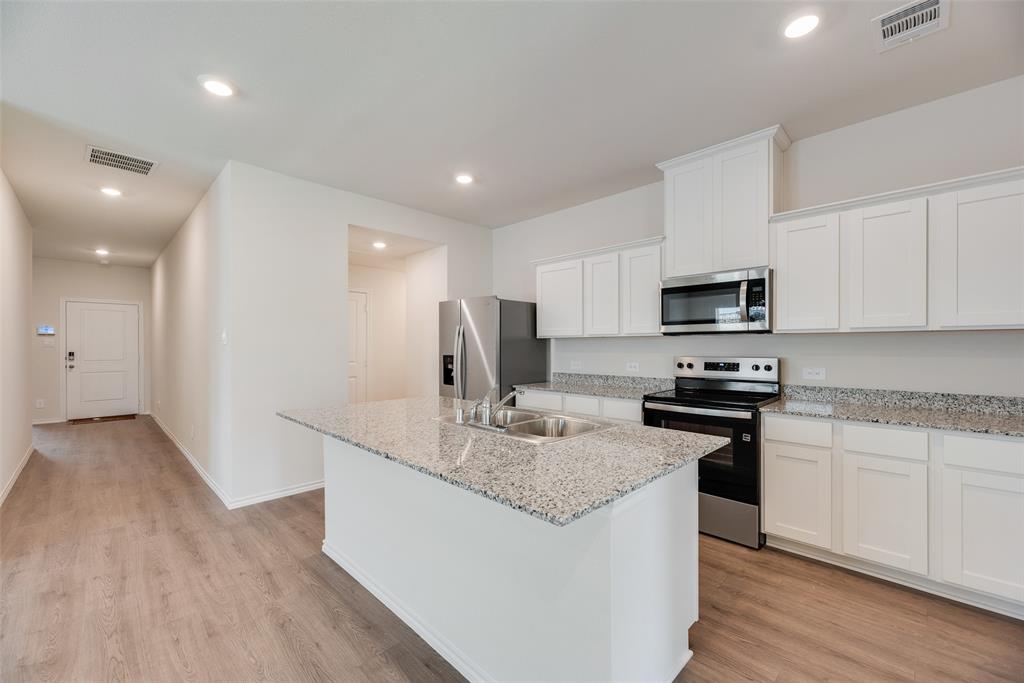 3407 Rendezvous Way Sherman, TX 75090 - Photo 7 of 17 Modern kitchen featuring a central island with a double basin sink, granite countertops, stainless steel appliances, white cabinetry, and wood-finish flooring