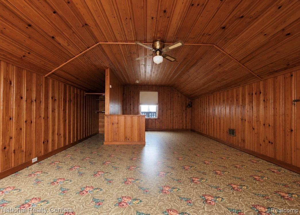 7285 Helen Street Center Line, MI 48015 - Photo 22 of 32 Room featuring wood-paneled walls and ceiling, a built-in partial wall structure, window, ceiling fan with integrated lighting, and patterned carpet flooring