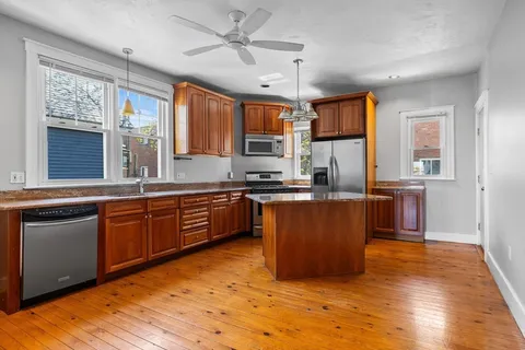 a large kitchen with stainless steel appliances granite countertop a stove a sink dishwasher a microwave oven and a dining table with wooden floor