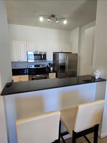 a living room with stainless steel appliances furniture a refrigerator and a kitchen view