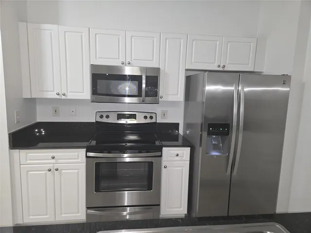 a kitchen with stainless steel appliances granite countertop a refrigerator stove and white cabinets