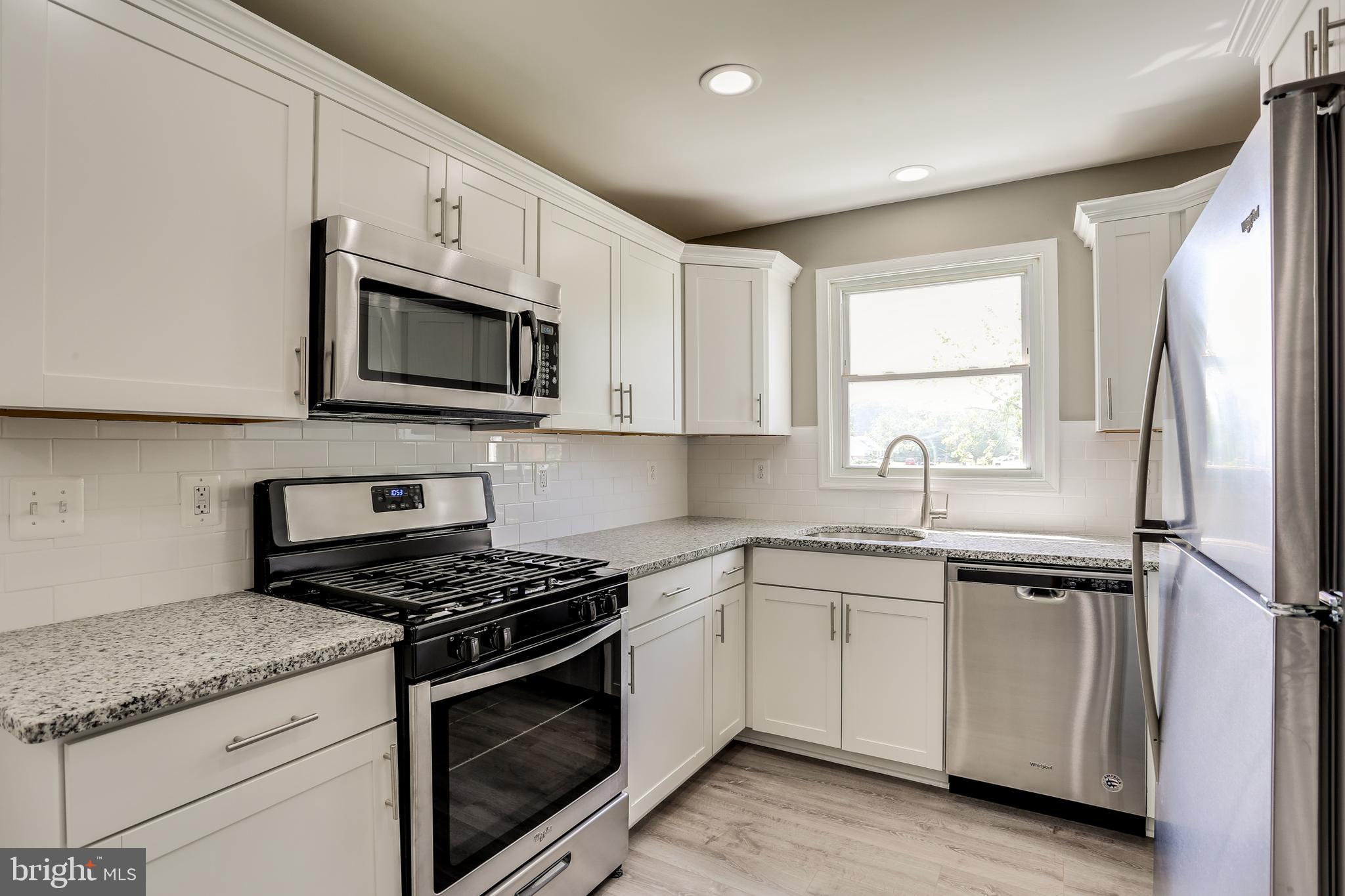 7106 Munford Road Baltimore, MD 21244 - Photo 11 of 31 a kitchen with stainless steel appliances granite countertop white cabinets a sink a stove a refrigerator and microwave with wooden floor