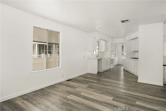 a view of empty room with wooden floor and kitchen