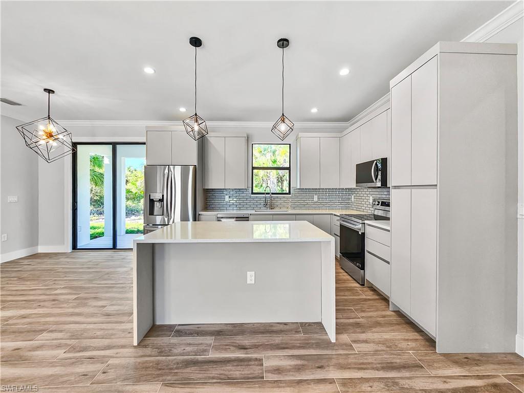2997 28th Avenue Southeast Naples, FL 34117 - Photo 9 of 49 a large kitchen with kitchen island a stove a sink dishwasher a refrigerator and a fireplace with wooden floor