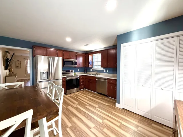 a kitchen with stainless steel appliances granite countertop a refrigerator a sink dishwasher a stove and a dining table with wooden floor