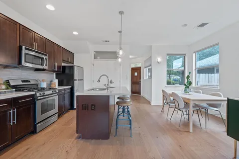 a kitchen with stainless steel appliances granite countertop a stove top oven a sink dishwasher a dining table and chairs with wooden floor