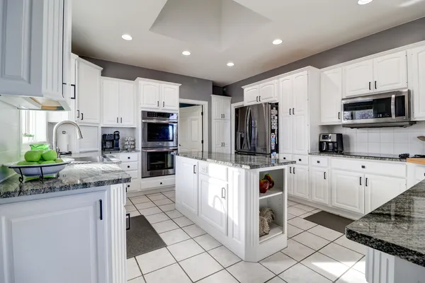 a kitchen with stainless steel appliances granite countertop a stove top oven a sink dishwasher a refrigerator and a oven with white cabinets