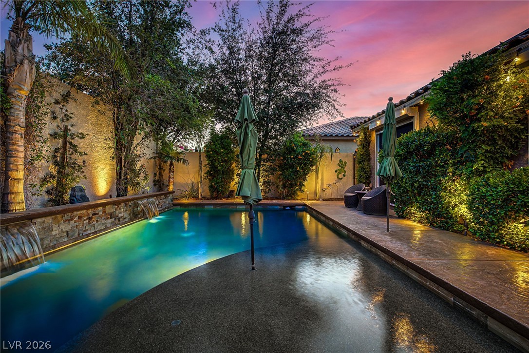 7415 Campbell Ranch Avenue Las Vegas, NV 89179 - Photo 48 of 52 An illuminated backyard oasis with a serene pool and cascading water features under a vibrant sunset.