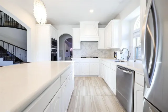 a kitchen with stainless steel appliances a sink a stove a refrigerator with white cabinets and wooden floor