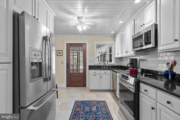 a kitchen with stainless steel appliances granite countertop a refrigerator a stove a sink and white cabinets
