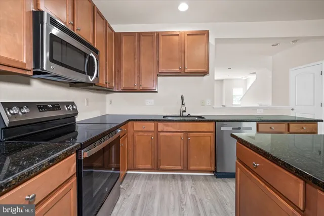 a kitchen with stainless steel appliances granite countertop wooden cabinets a stove a sink and dishwasher with wooden floor