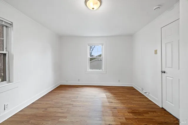 a view of an empty room with wooden floor and window