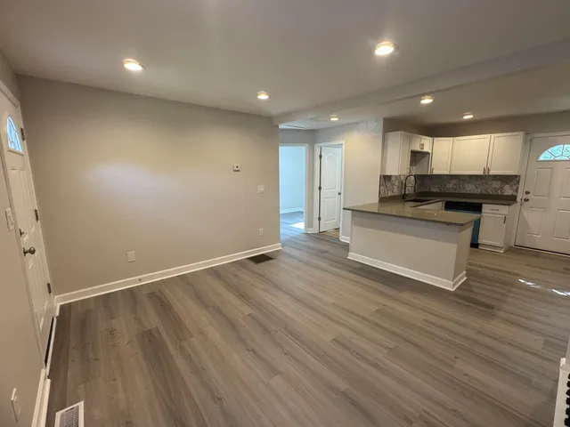 an empty room with wooden floor and kitchen view