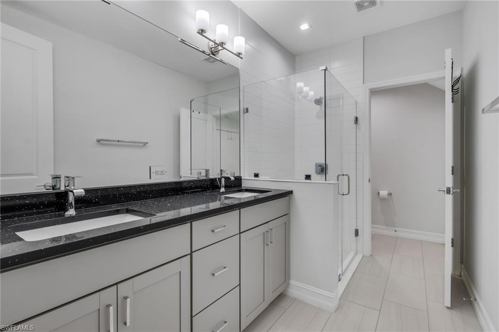7501 Carnegie Way Naples, FL 34119 - Photo 20 of 37 Full bathroom featuring a stall shower, double vanity, and light tile patterned flooring
