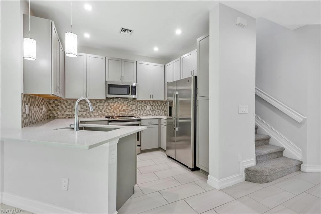7501 Carnegie Way Naples, FL 34119 - Photo 4 of 37 Kitchen featuring hanging light fixtures, stainless steel appliances, light stone counters, backsplash, and light tile patterned floors