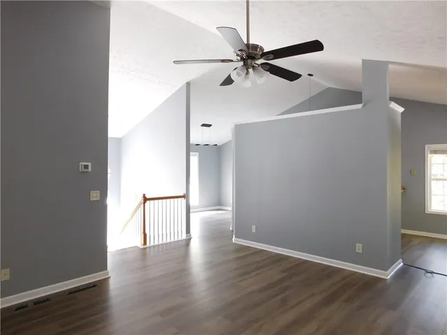 an empty room with wooden floor fan and windows