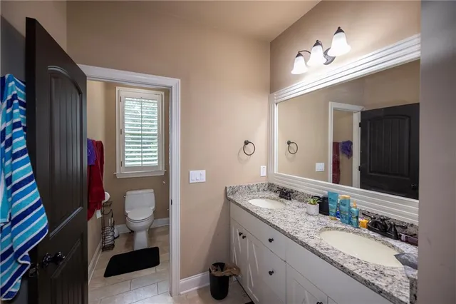 a bathroom with a granite countertop double vanity sink a mirror and a toilet