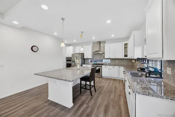 a kitchen with stainless steel appliances granite countertop a stove top oven a sink dishwasher and a refrigerator with wooden floor