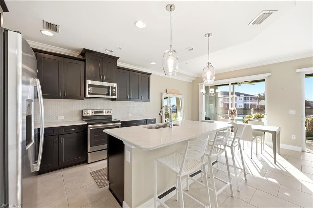 6980 Avalon Circle, Unit 1102 Naples, FL 34112 - Photo 5 of 24 Kitchen featuring stainless steel appliances, backsplash, light stone counters, a breakfast bar area, and hanging light fixtures