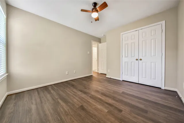 an empty room with wooden floor ceiling fan and windows