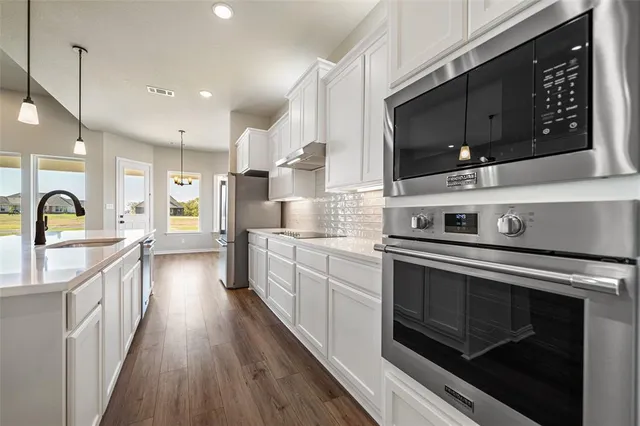 a kitchen with stainless steel appliances granite countertop a refrigerator a sink and white cabinets