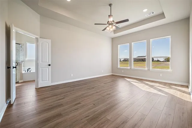 an empty room with wooden floor chandelier fan and windows
