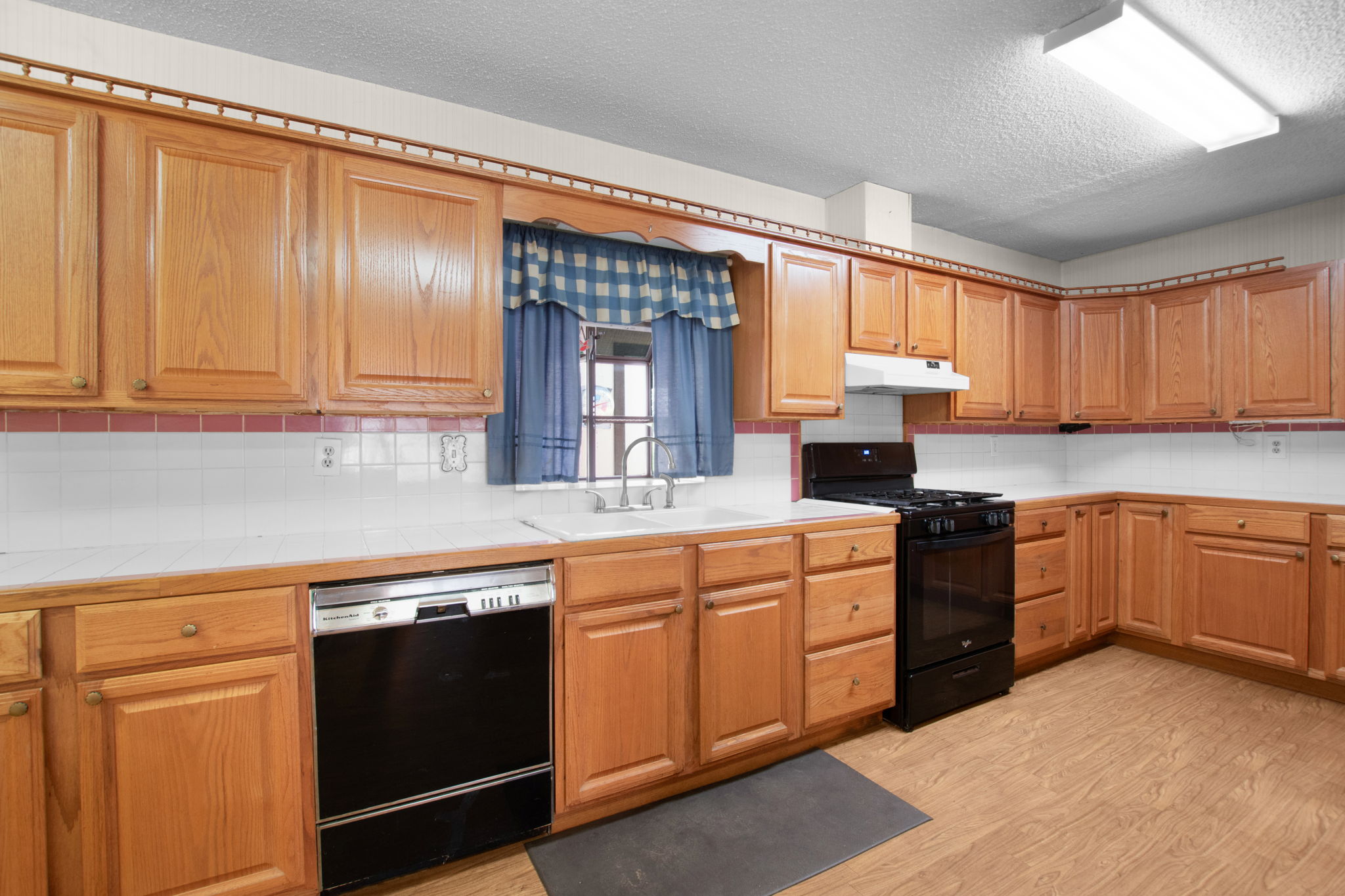 112 Frazier Tow, TX 78672 - Photo 6 of 30 Kitchen featuring light wood finished floors, under cabinet range hood, tile countertops, a sink, and black appliances