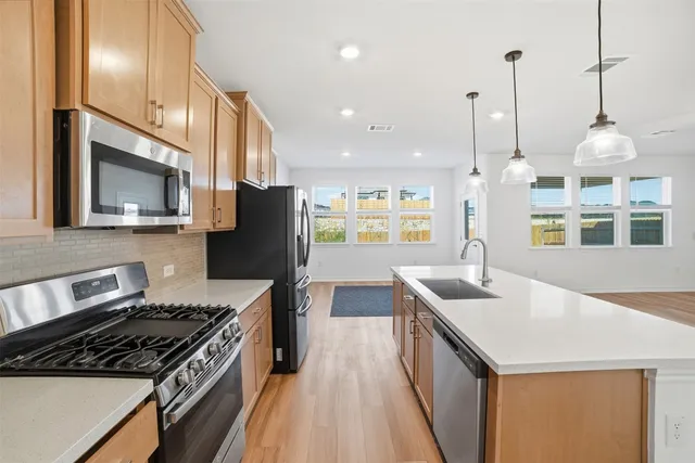 a kitchen with stainless steel appliances kitchen island granite countertop a stove a sink a refrigerator and white cabinets with wooden floor