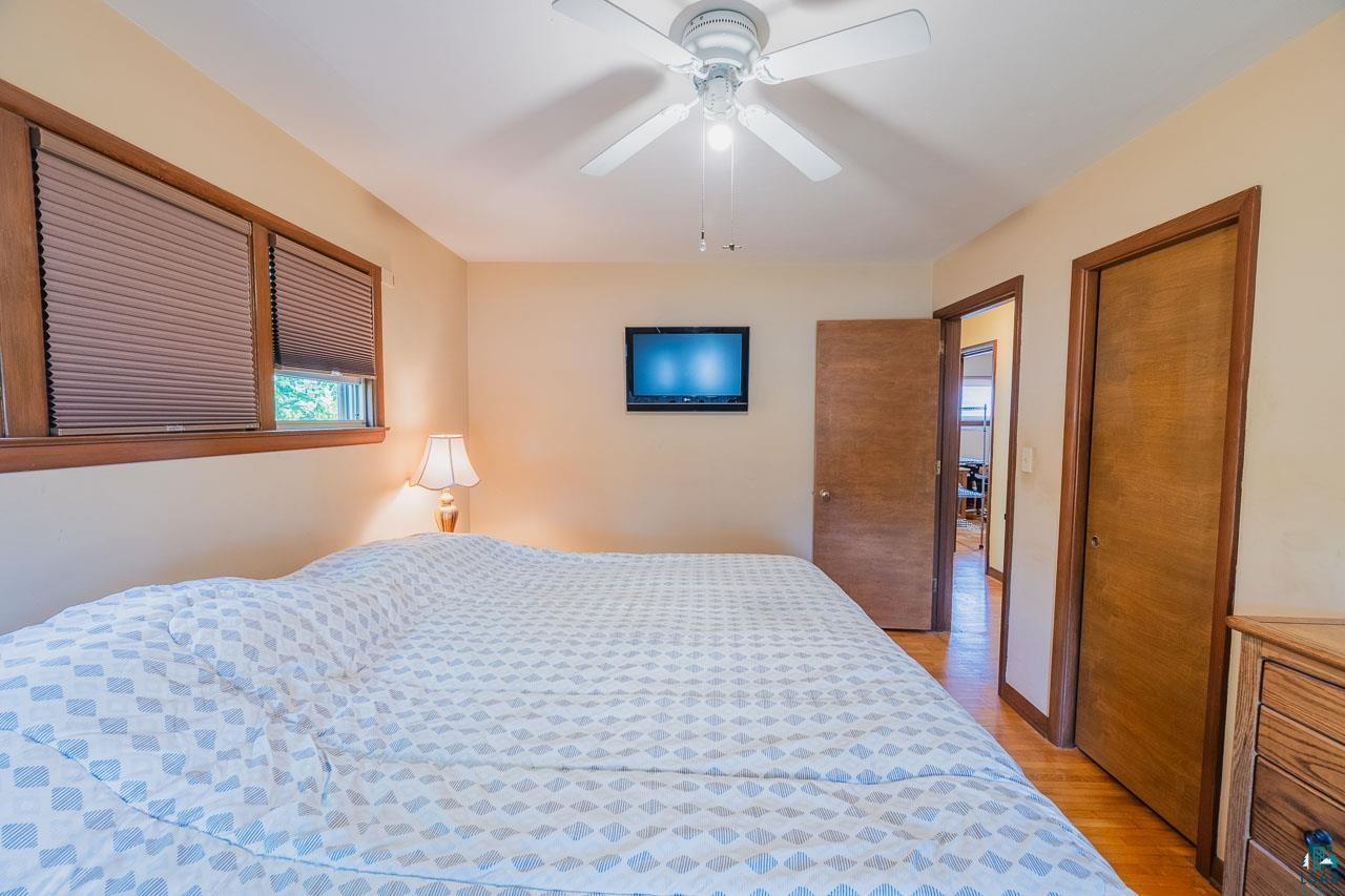 101 2nd Avenue North Biwabik, MN 55708 - Photo 14 of 44 Bedroom featuring wood-finish flooring, two large windows with horizontal blinds, a ceiling fan with integrated lighting, and two wood-paneled doors