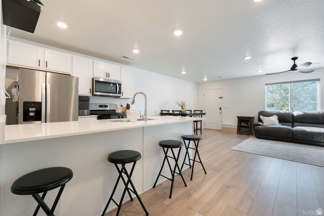 1693 Devils Gdn Lane Washington, UT 84780 - Photo 11 of 64 Open-concept kitchen and living area featuring white cabinetry, stainless steel appliances, a kitchen island with seating, recessed lighting, and wood-finish flooring
