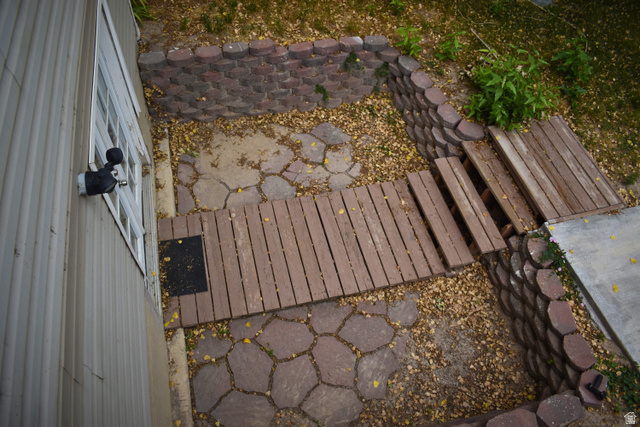 3327 East Windhover Road Eagle Mountain, UT 84005 - Photo 34 of 38 Landscaped outdoor area featuring a patterned paver pathway, wood-plank walking surfaces, and stacked stone retaining walls