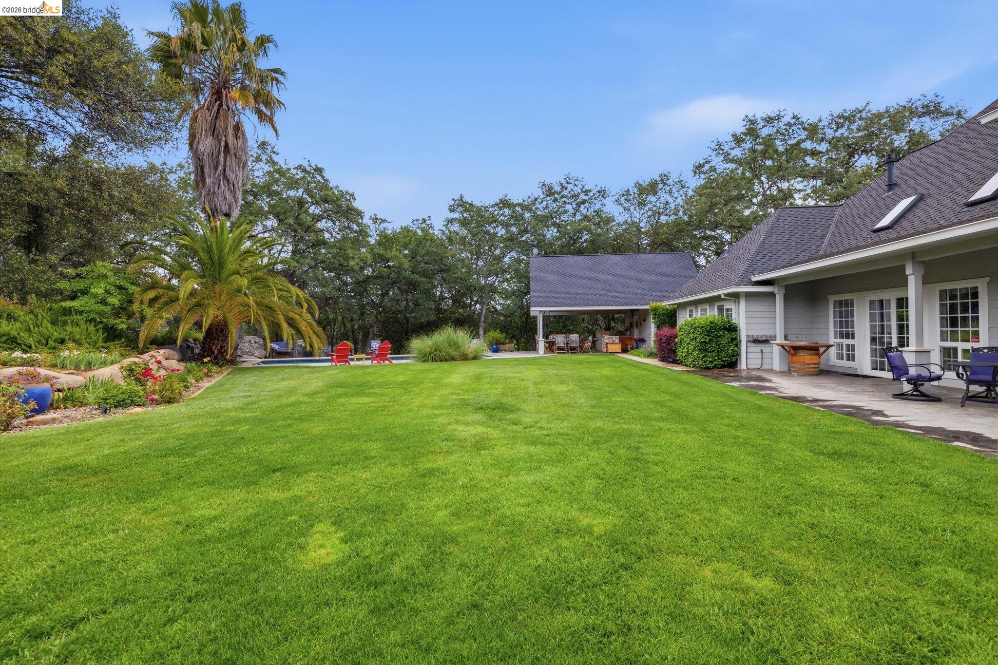 18450 Lambert Lake Road Sonora, CA 95370 - Photo 12 of 87 Expansive green lawn bordering a stucco exterior home with multiple French doors