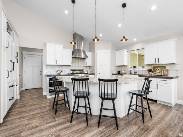 7 Sterling Loop Vineyard, UT 84059 - Photo 13 of 43 Bright kitchen featuring white cabinetry, a large kitchen island with seating, wood-finish flooring, a stainless steel range hood, and pendant lighting