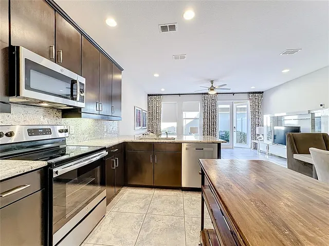 a open kitchen with stainless steel appliances granite countertop a stove top oven a sink dishwasher a dining table and chairs with wooden floor