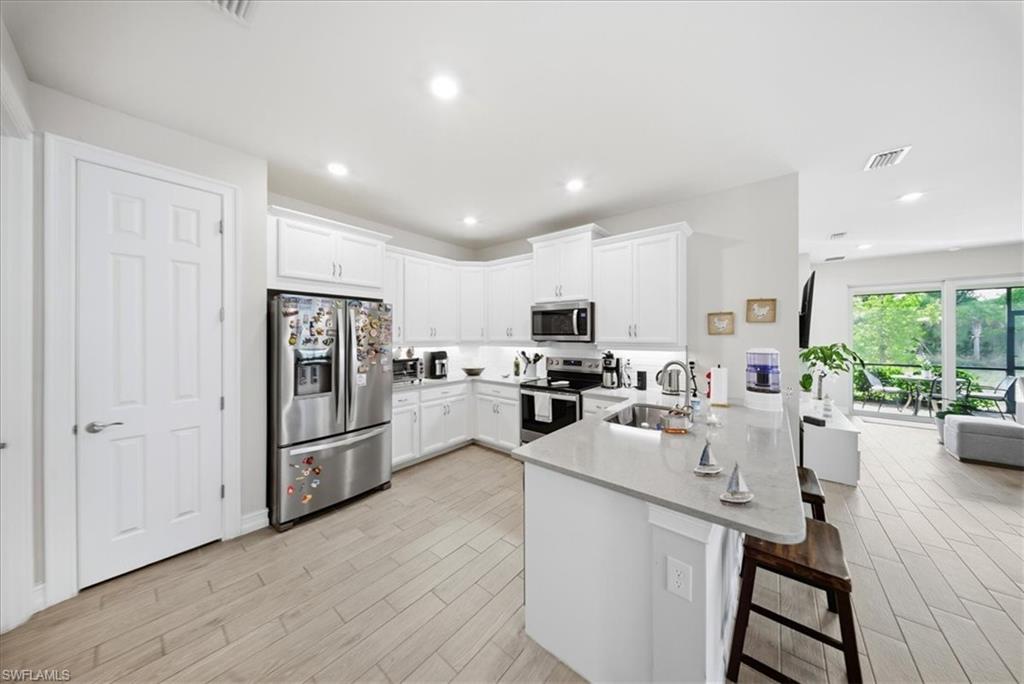 1074 Enbrook Loop Naples, FL 34114 - Photo 9 of 36 a kitchen with stainless steel appliances a refrigerator a stove a sink dishwasher a oven with white cabinets and wooden floor