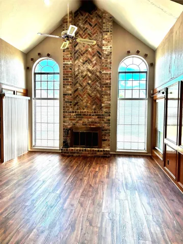 an empty room with wooden floor fireplace and windows