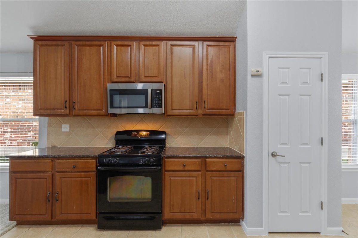 17812 Masi Loop Pflugerville, TX 78660 - Photo 11 of 38 Kitchen featuring wood-finish cabinetry, stainless steel microwave, black gas range, and a tiled backsplash