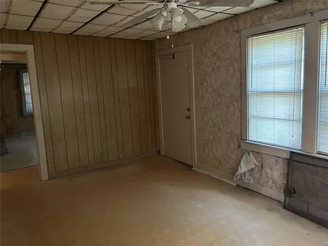 an empty room with chandelier fan and kitchen view