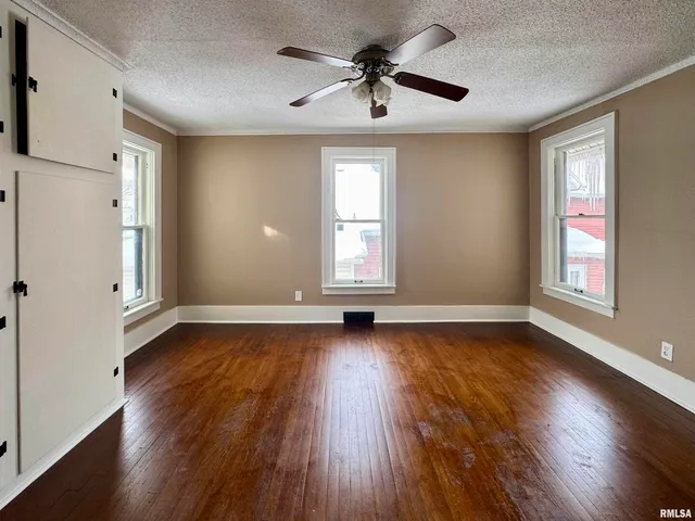 an empty room with wooden floor chandelier fan and windows