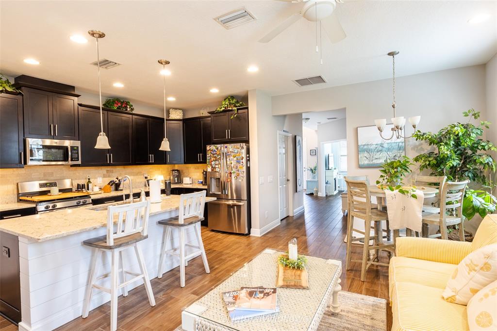 12556 Rangeland Boulevard Odessa, FL 33556 - Photo 9 of 29 a kitchen with stainless steel appliances kitchen island granite countertop a refrigerator oven a sink a dining table and chairs with wooden floor