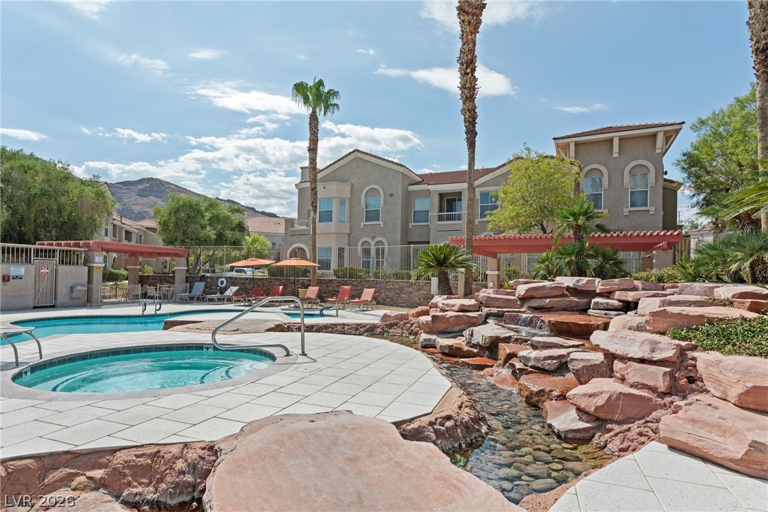 10550 West Alexander Road, Unit 1025 Las Vegas, NV 89129 - Photo 34 of 42 A tranquil oasis featuring a sparkling pool, relaxing spa, and a natural rock waterfall, all framed by desert landscaping and distant mountains.