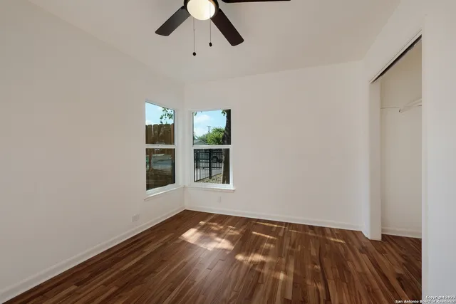 an empty room with wooden floor cabinet and windows
