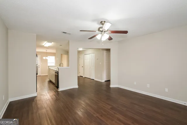 a view of an empty room with wooden floor and a kitchen