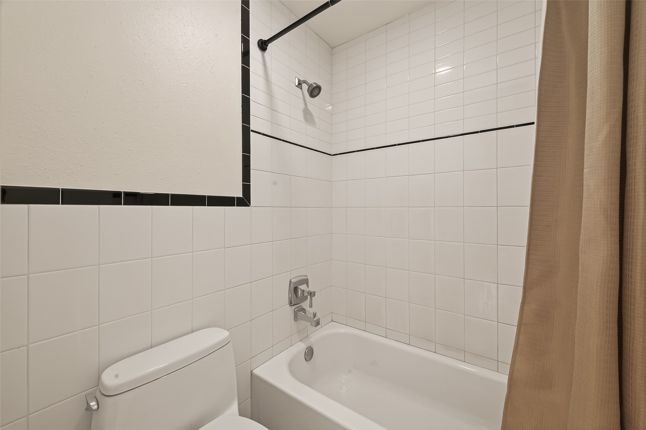 2829 Timmons Lane, Unit 144 Houston, TX 77027 - Photo 22 of 41 Classic white-tiled shower and bathtub, featuring a black trim accent.