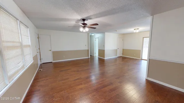 an empty room with wooden floor chandelier fan and windows