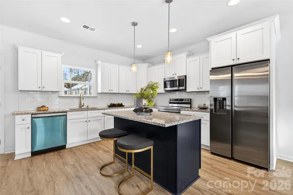 a kitchen with kitchen island granite countertop stainless steel appliances a sink a stove a refrigerator cabinets and dining table