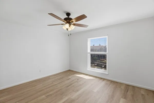 an empty room with wooden floor fan and windows