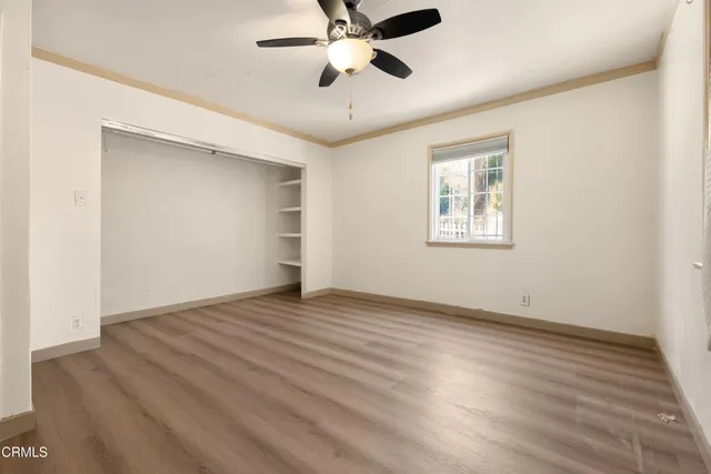 an empty room with wooden floor ceiling fan and windows